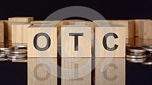 OTC - text on wood blocks on black background with coins. front view. business concept