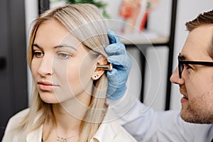 Otolaryngologist doctor checking young woman's ear using otoscope or auriscope at ENT clinic, close up. Hearing exam