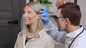 Otolaryngologist doctor checking young woman's ear using otoscope or auriscope at ENT clinic. Hearing exam