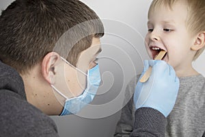 An otolaryngologist examines a child`s throat with a wooden spatula. A possible diagnosis is inflammation of the pharynx, tonsils