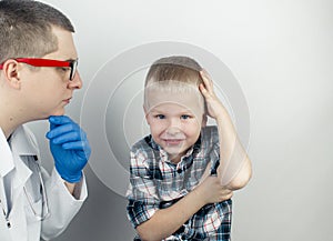 An otolaryngologist examines the ear of a boy who complains of pain. Pain relief and treatment concept. Inflammation of the ear
