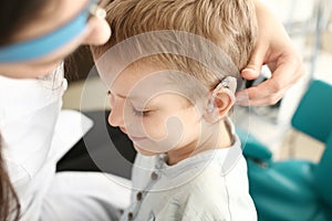 Otolaryngologist putting hearing aid in little boy's ear indoors