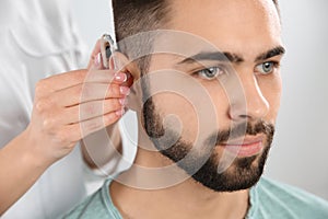 Otolaryngologist putting hearing aid in man`s ear on white