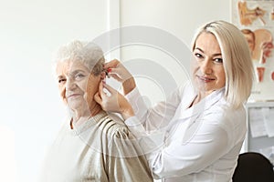 Otolaryngologist putting hearing aid in senior woman's ear indoors