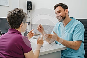 Otolaryngologist showing Modern miniature hearing aids at hospital for woman