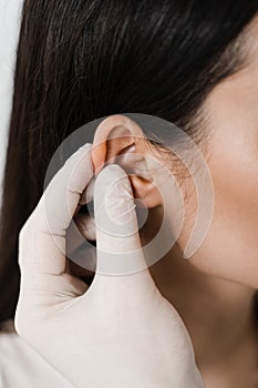 Otoplasty ear surgery close-up. Surgeon doctor examines girl ears before otoplasty cosmetic surgery. Otoplasty surgical