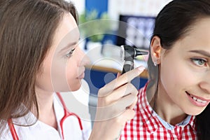 Otorhinolaryngologist examines patient ear with otoscope closeup photo