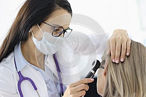 Otorhinolaryngologist looking at female patients ear with otoscope in clinic photo