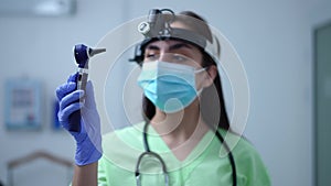 Otoscope in hand of blurred Caucasian female otolaryngologist standing in hospital indoors. Young Caucasian woman in