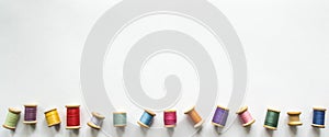 Ots of multicolored threads on old-fashioned wooden reels on a white background with space for text. One of the thread reels is