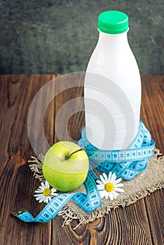 Ottle of kefir, green apple and tape measure on dark wooden background. Diet and slim concept