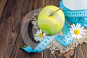 Ottle of kefir, green apple and tape measure on dark wooden background. Diet and slim concept