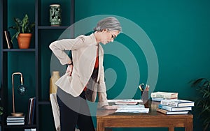 Ouch My back. an attractive mature businesswoman standing and suffering from backache while in her home office.