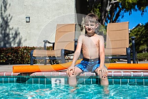 Oudoor summer activity. Concept of fun, health and vacation. Boy eight years old sits near a pool in hot summer day.