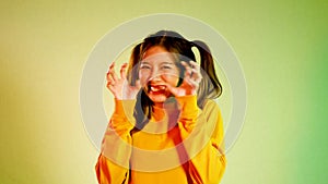 oung asian girl in yellow sweatshirt cute posing on the yellow neon screen background. 4K video asia woman