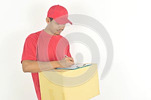 Oung delivery man holding box and writing something on clipboard