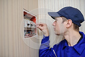 Oung electrician in blue overall disassembling a electrical panel