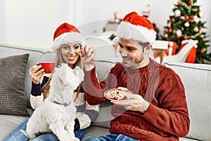 oung hispanic couple wearing christmas hat drinking coffee and eating cookies