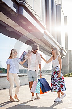Oung man carrying all the bags while two girlfriends are laughing and joking by his side