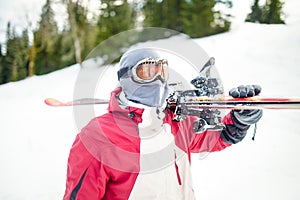Oung man holding ski.Skier holding skis looking at the mountains.Side view of handsome skier man with mask and holding ski equipme