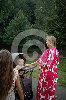 Oung mother walks with a little toddler in a stroller in the summer on nature