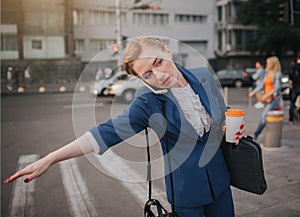 Oung stylish businesswoman with coffee cup catching a taxi. Woman doing multiple tasks. Multitasking business woman.