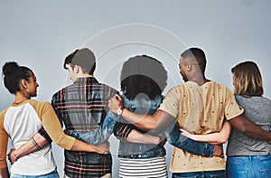 Our friends become our family. Rearview studio shot of a diverse group of young people embracing each other against a