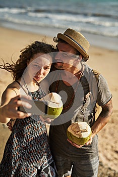 Our friends will be so jealous. a happy young couple taking selfies while enjoying cocktails on the beach.