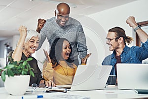 Our hard work is paying off. a group of cheerful businesspeople looking at a laptop screen together while cheering in