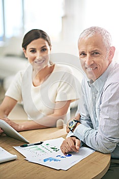 Our hard work is paying off. Portrait of two coworkers sitting at a table discussing paperwork while using a digital