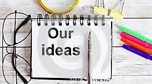 OUR IDEAS written in a notebook on white background with office tools