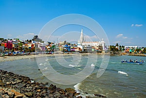 Our Lady of Ransom Shrine Church behind colorful houses on a sand beach occupied by fishing boats in Kanyakumari in India