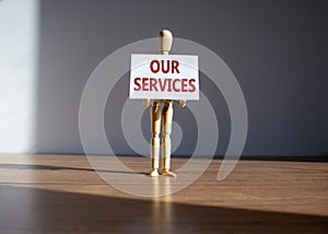 Our services symbol. Wooden model of human holding a white paper with words `our services`. Beautiful wooden table, white