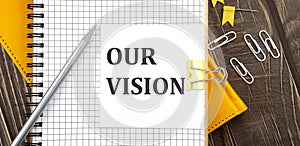 OUR VISION text on a sticker on the notebook, wooden background