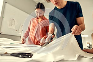 Out of the best materials. Cropped shot of young male designer cutting white fabric textile in a studio. Group of