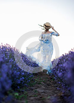 Out of focus. Blurred silhouette of a woman with hat wearung white dress running on a lavender field. view from the back