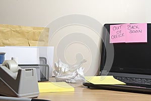 Out of office, back soon message left on a messy office desk