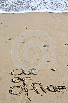Out of office text written in sand on a beach