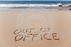 Out of office written in the sand on a beach