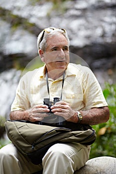 Out watching for birds. a senior man with binoculars looking at the scenery.