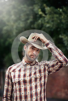 Out west its all about how you wear your attitude. a handsome cowboy wearing a check shirt and stetson.