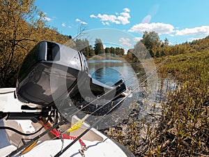 outboard motor in a boat and spinning rods next to the background of the river and sky