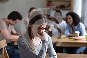 Outcast girl sitting separately by others teenagers in cafe photo