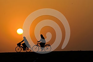 outdoor activities. two people in the burqa ride bicycles against the morning sunrise photo