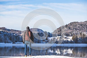 Outdoor adventure: Caucasian man is standing at the lakeshore and enjoys the view. Beautiful winter landscape, Austria