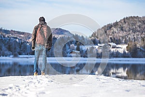 Outdoor adventure: Caucasian man is standing at the lakeshore and enjoys the view. Beautiful winter landscape, Austria