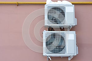An outdoor air conditioner unit installed on the outer wall of a residential building close-up. Operation of the air conditioner