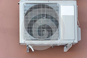 An outdoor air conditioner unit installed on the outer wall of a residential building. The fan and the radiator grille of the air