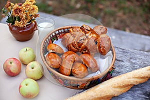 Outdoor autumn picnic on old table. Beautiful rustic picnic composition with with bread, a buns, applesand bouquet of flowers on w