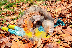 Outdoor autumn portrait of little girl and boy laying in autumn park. Fall leaves relaxing and still life kids concept.